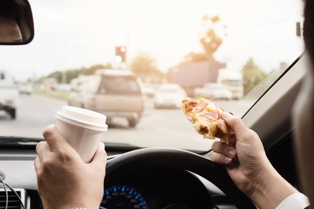 Someone driving a car drinking coffee and eating pizza.