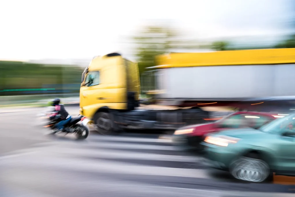 A blurred image of a motorcycle about to get hit by a commercial truck.