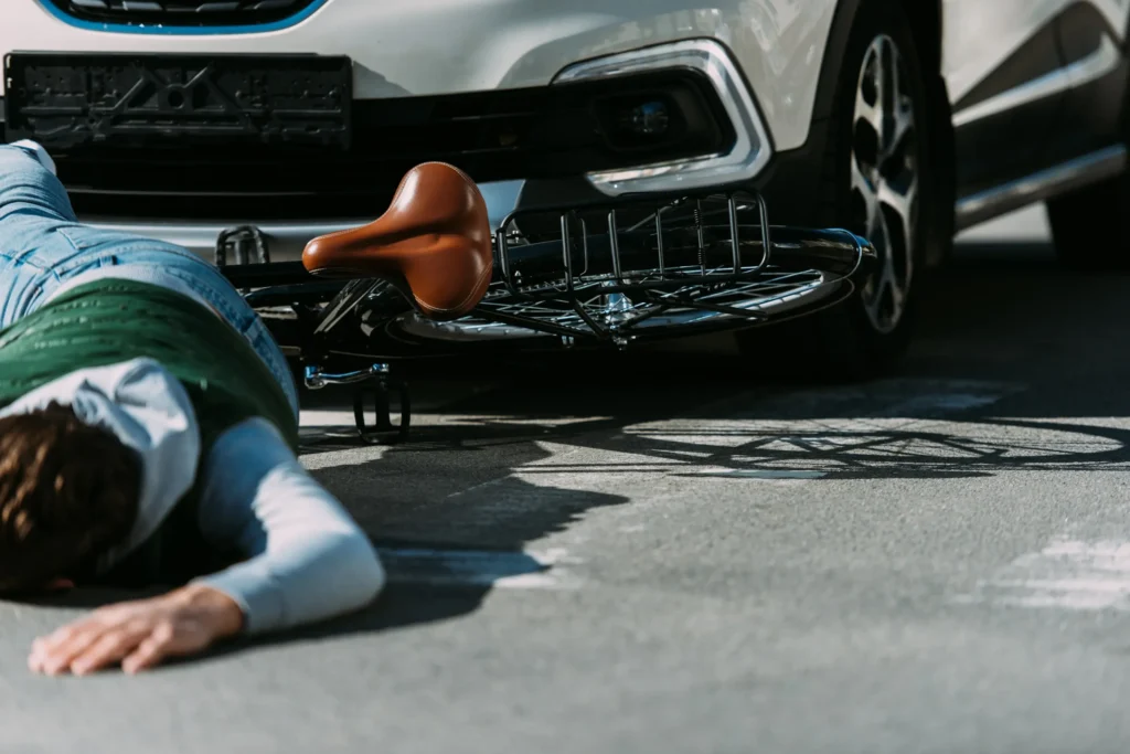 A man laying on the ground next to his bike after being hit by a car.